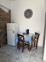 Un pequeño comedor con una mesa, dos sillas, un reloj en la pared, un refrigerador y una pared de piedra.
