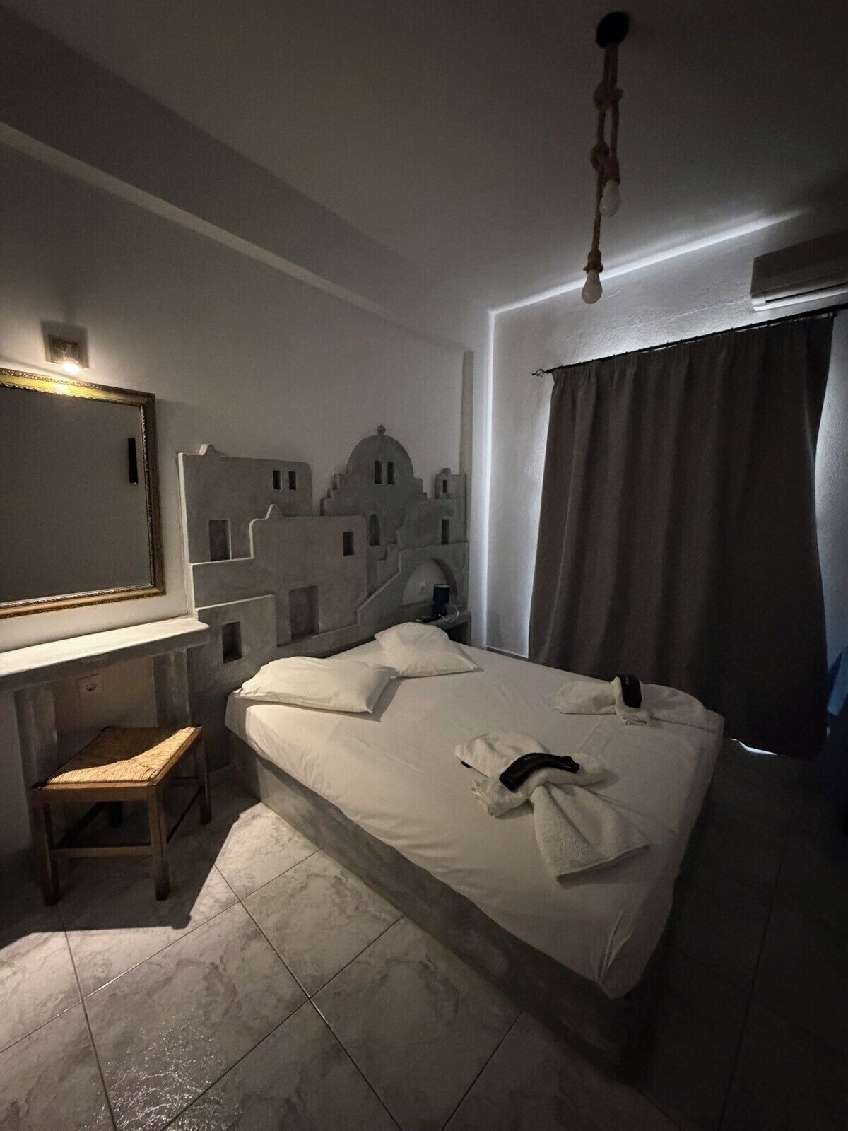 A hotel room with a bed, a desk, a chair, a mirror, and a wall decoration.