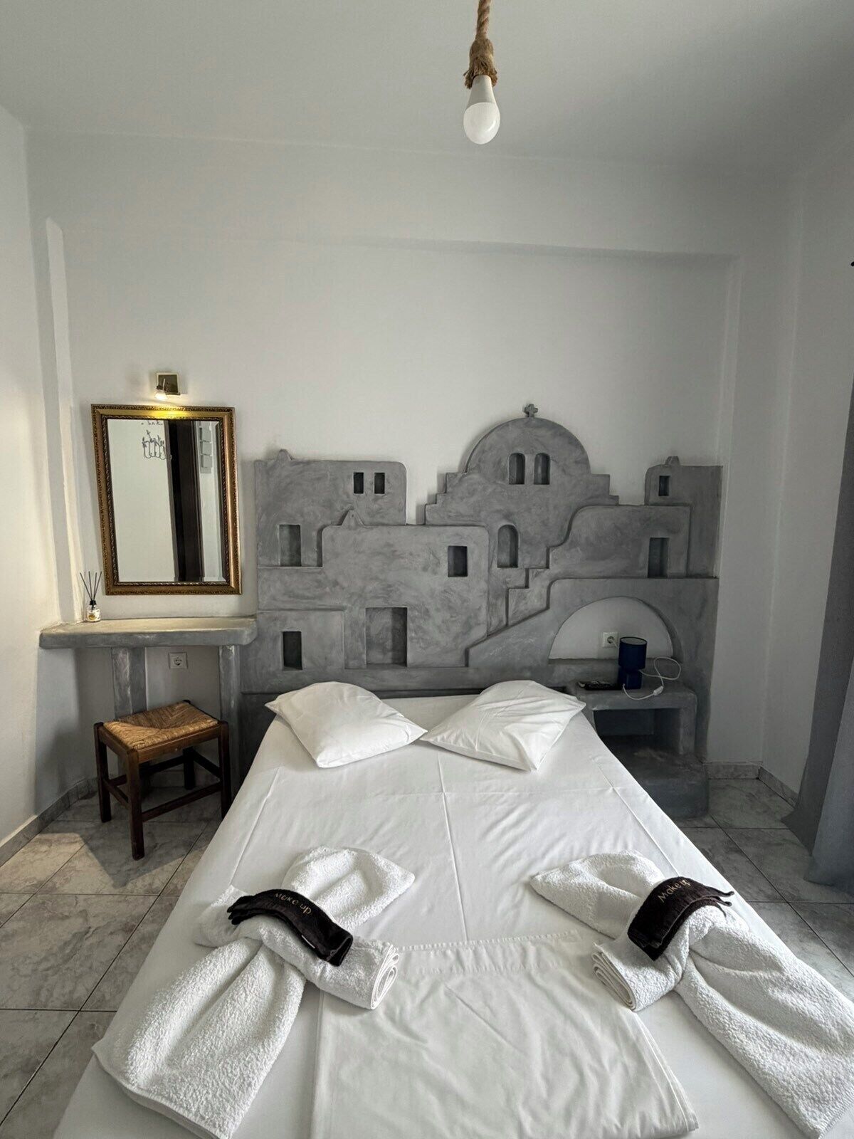 Ein Hotelzimmer mit einem Bett, einem Nachttisch, einem Sessel, einem Spiegel und einer Wandleuchte.