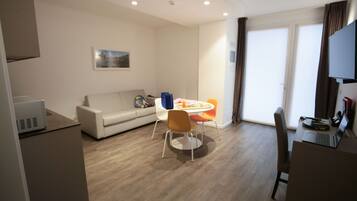 A modern living room with a sofa, a dining table with chairs, a flat-screen TV, and a laptop on a desk.