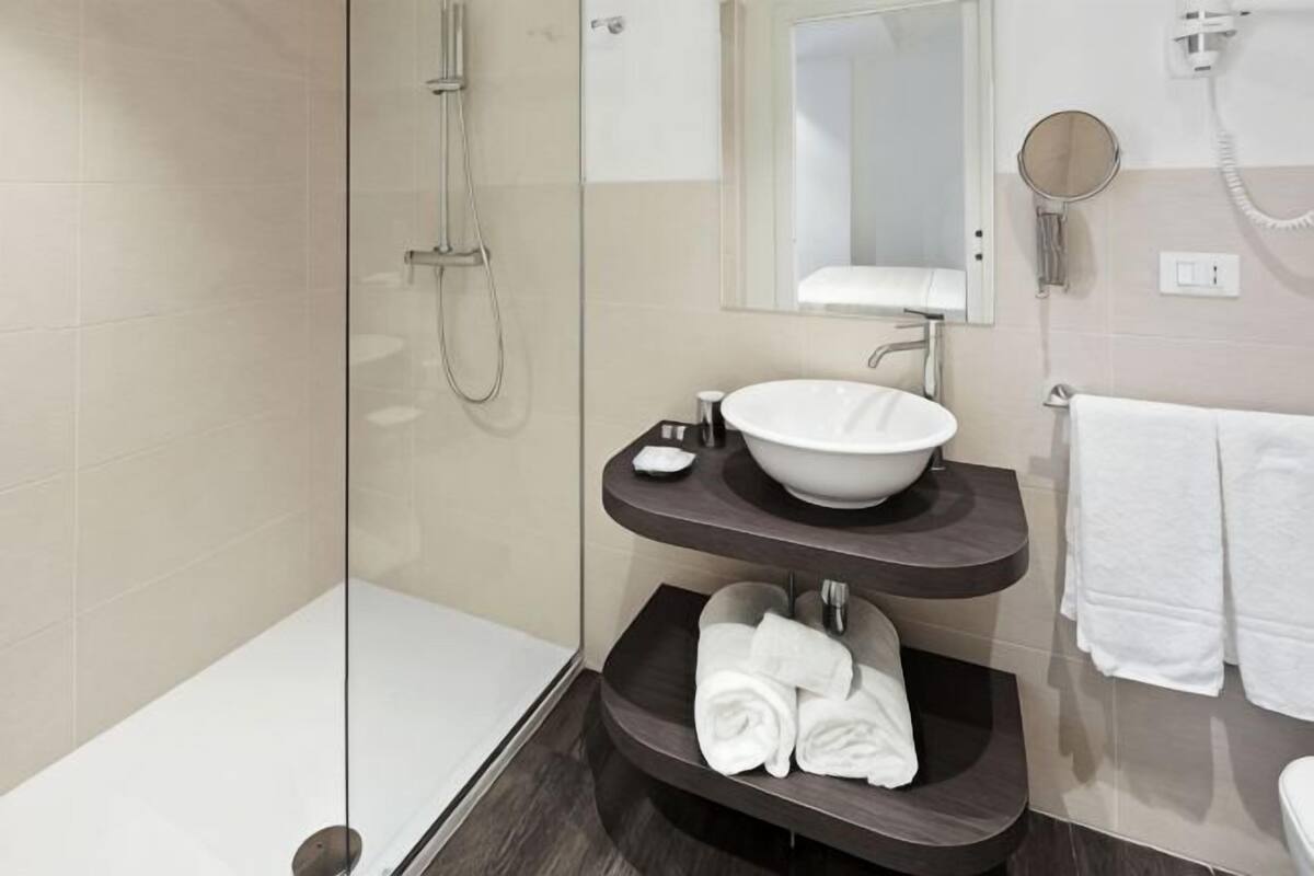 A modern bathroom with a glass-enclosed shower, a white sink with a round mirror, and a dark countertop.