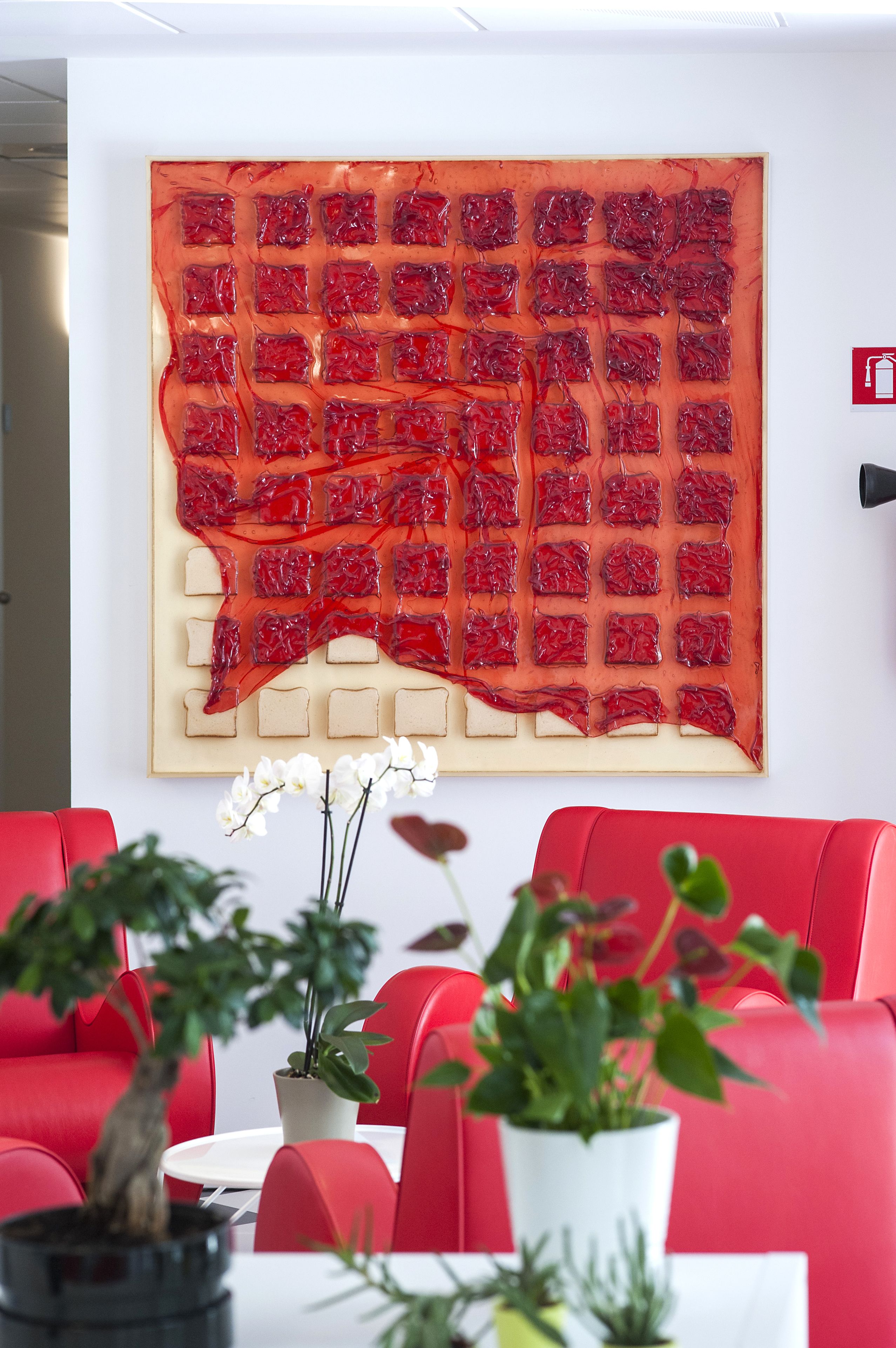 Ein modernes Interieur mit einer roten Sitzecke, einem großen abstrakten Kunstwerk an der Wand und Zimmerpflanzen.