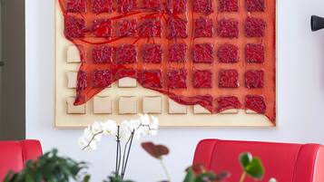 Ein modernes Interieur mit einer roten Sitzecke, einem großen abstrakten Kunstwerk an der Wand und Zimmerpflanzen.