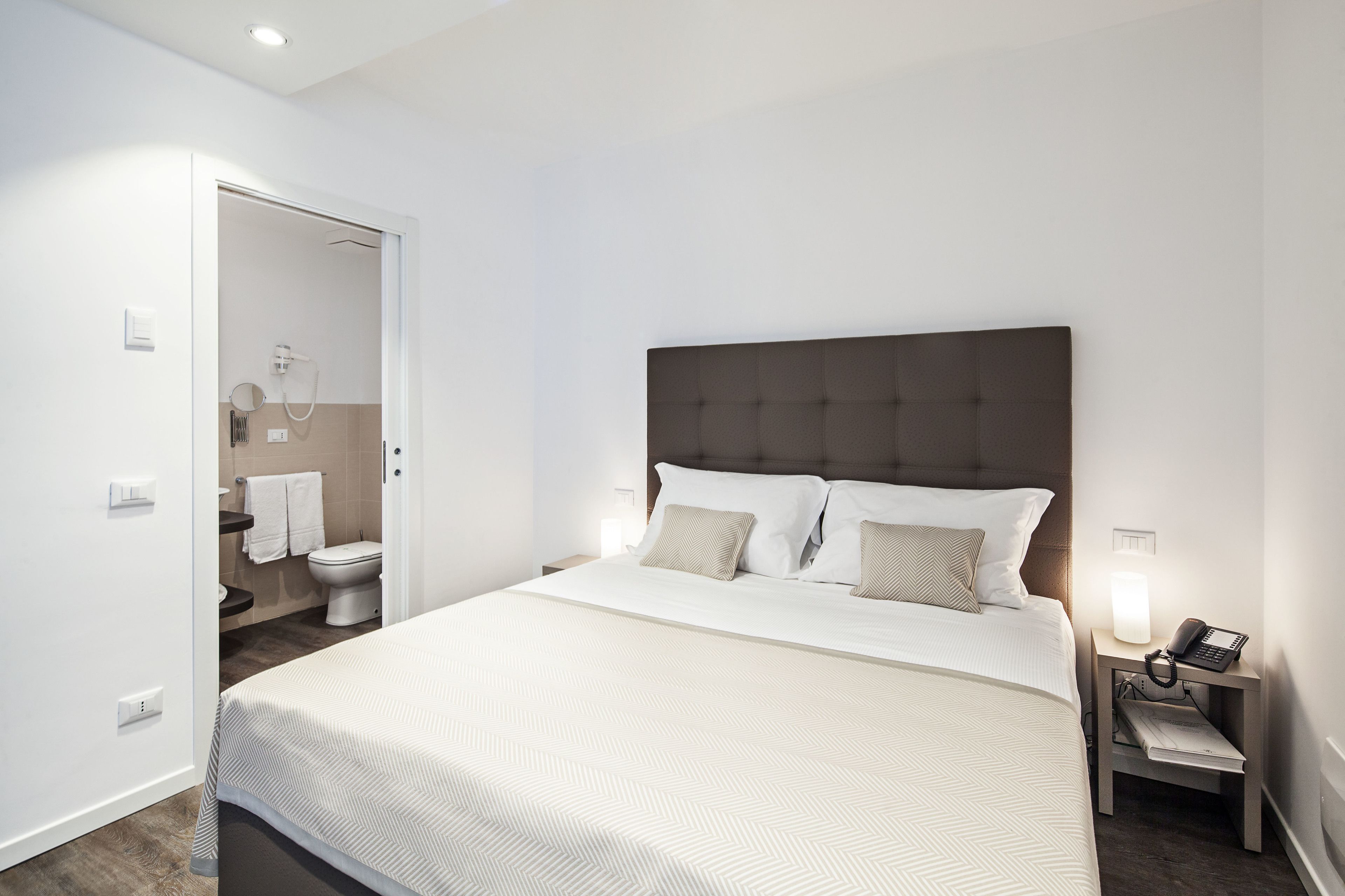 Una camera d'albergo moderna con un letto grande, un comodino con una lampada e vista sul bagno.