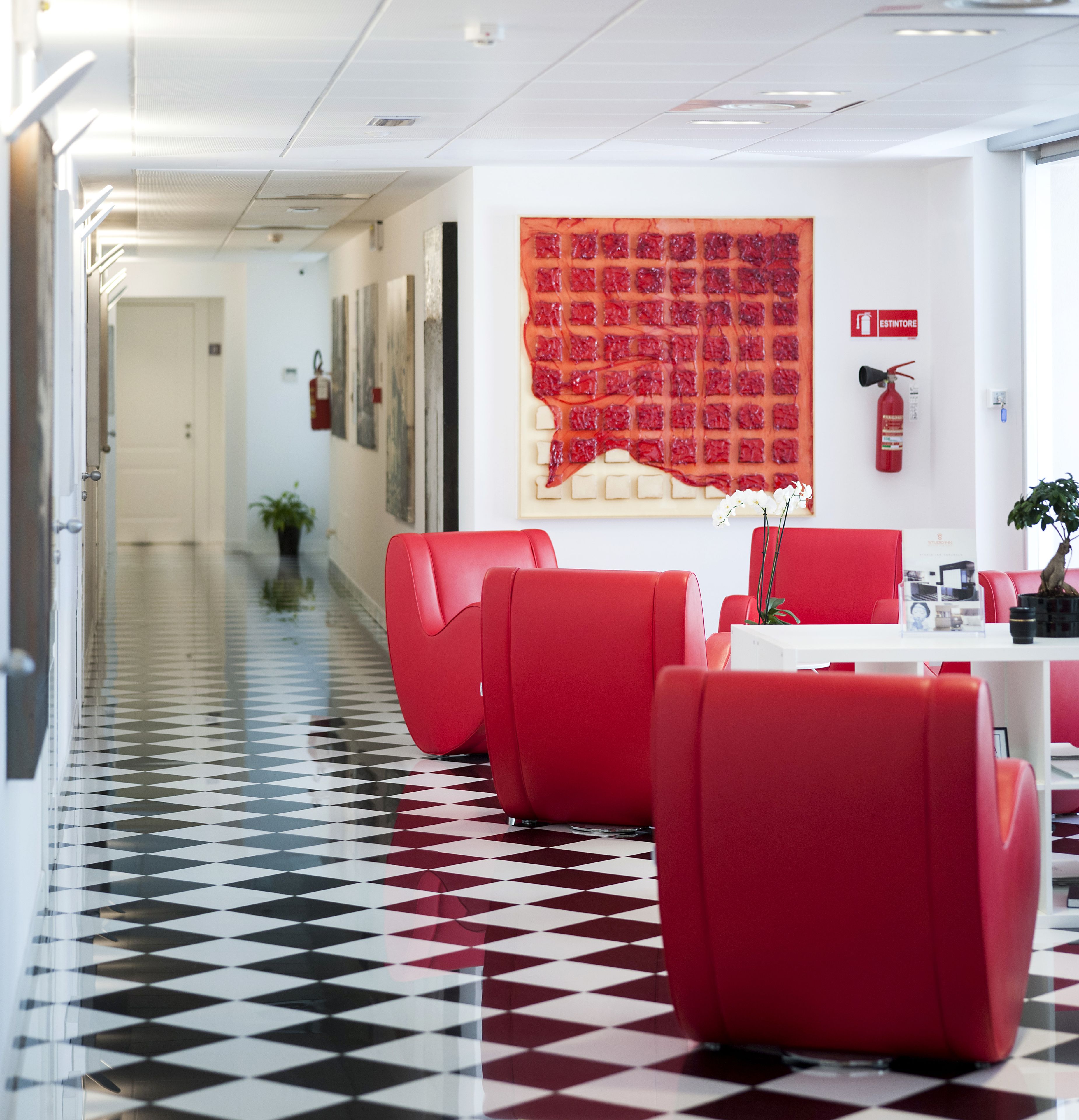 A hotel lobby with a checkered floor, red seating, and a large red artwork on the wall.
