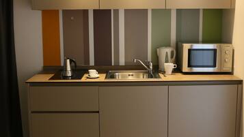 Una kitchenette compacta con microondas, hervidor y pileta.