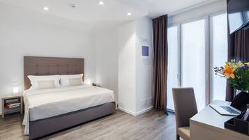 Una habitación de hotel moderna con una cama grande, un escritorio con una computadora portátil, un televisor y una ventana con cortinas.