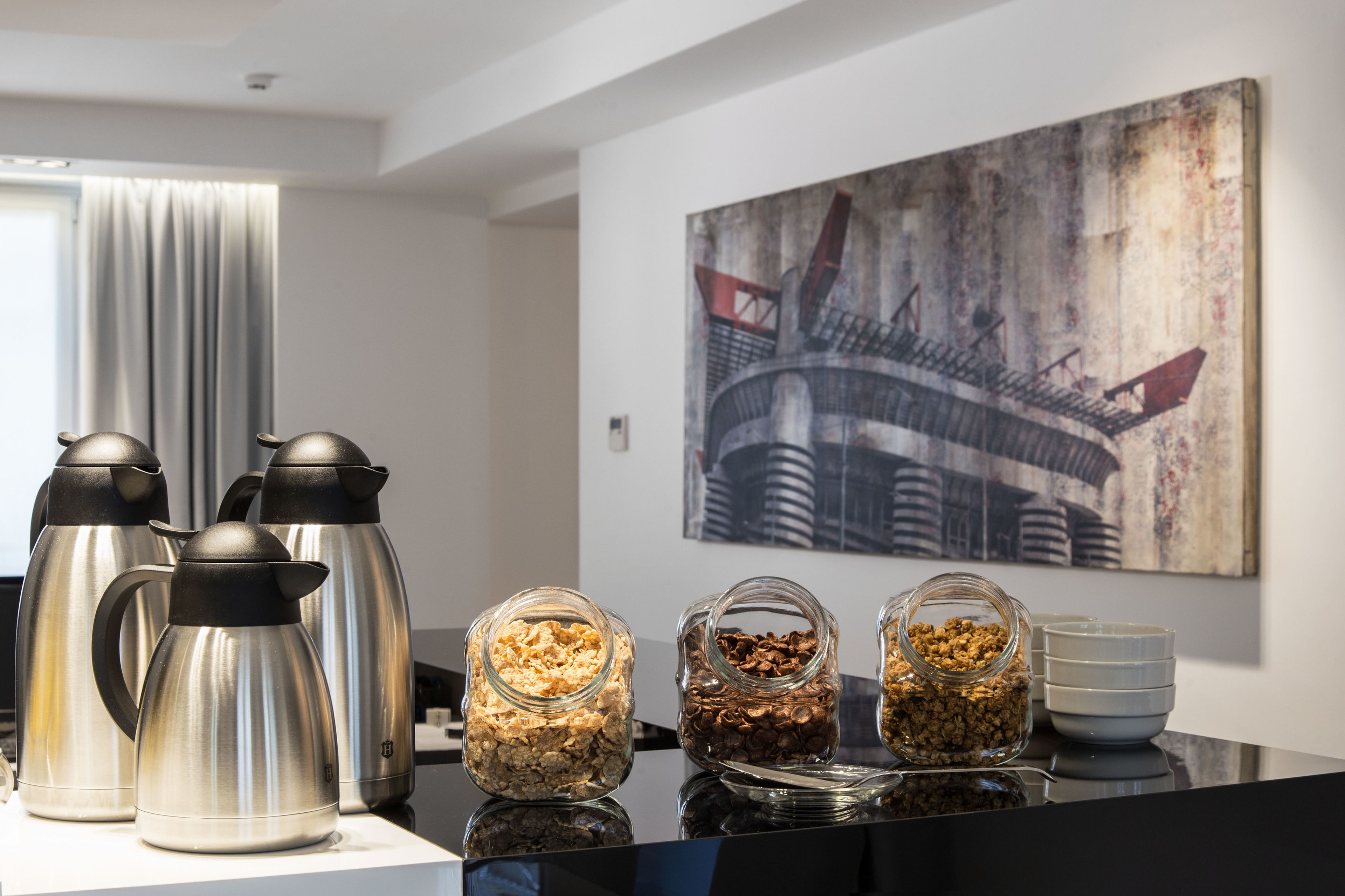 A breakfast setup with stainless steel coffee makers and glass jars of granola and nuts on a reflective surface.