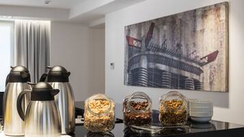 A breakfast setup with stainless steel coffee makers and glass jars of granola and nuts on a reflective surface.