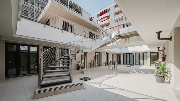 A spacious atrium with a central spiral staircase, multiple balconies, and potted plants. - Hotel Studio Inn Centrale & Milano Urban Padel (Milan)