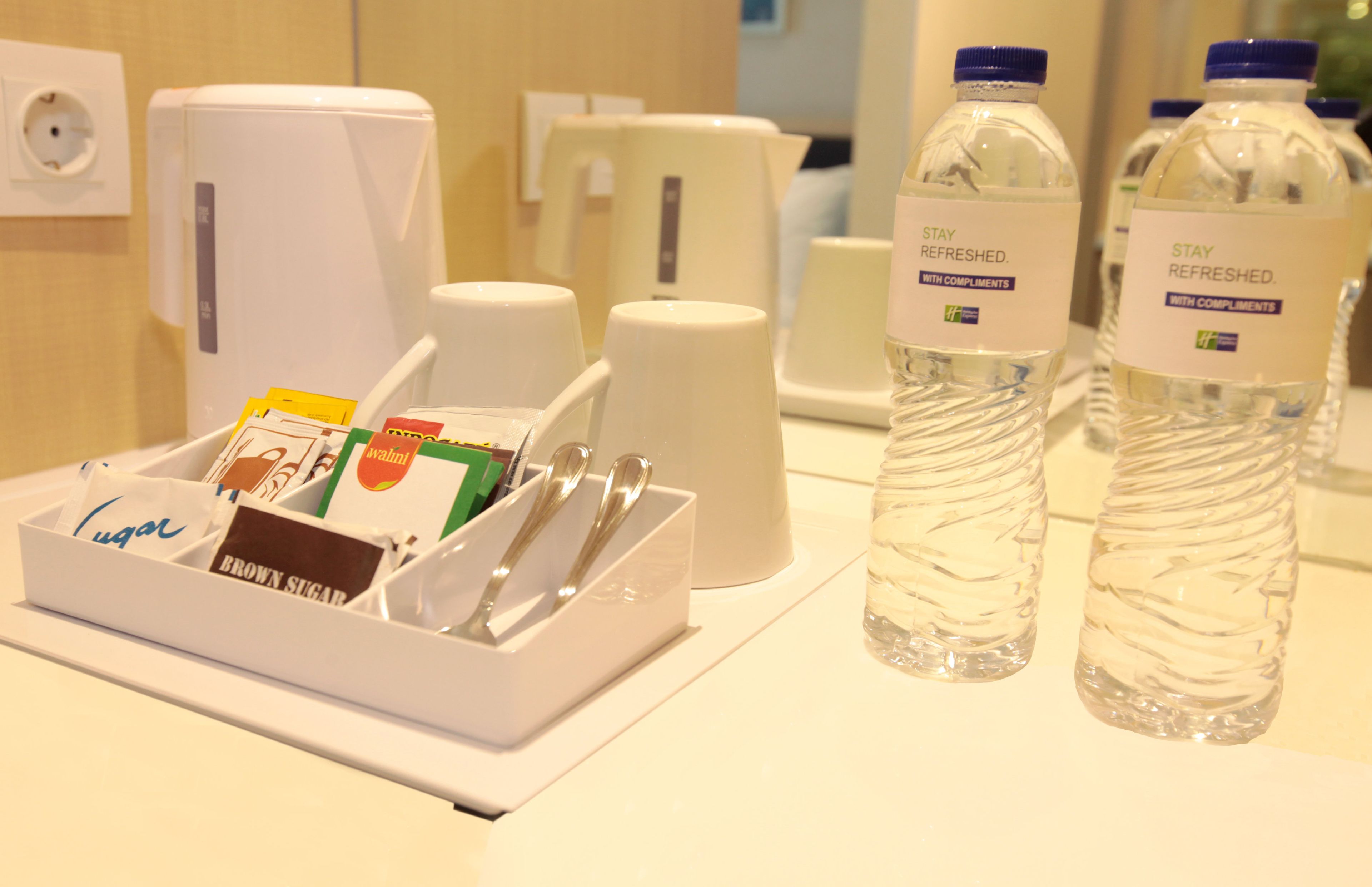 A hotel room's amenities area with a sugar packet holder, a coffee maker, and two water bottles.