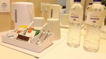 A hotel room's amenities area with a sugar packet holder, a coffee maker, and two water bottles.