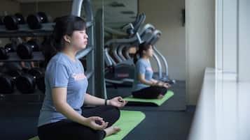 A person meditating on a green mat in a gym with exercise equipment in the background.