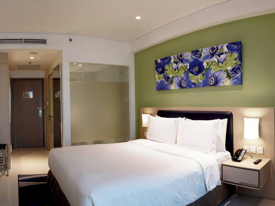 A hotel room with a bed, a desk, a chair, a TV, and a painting on the wall.