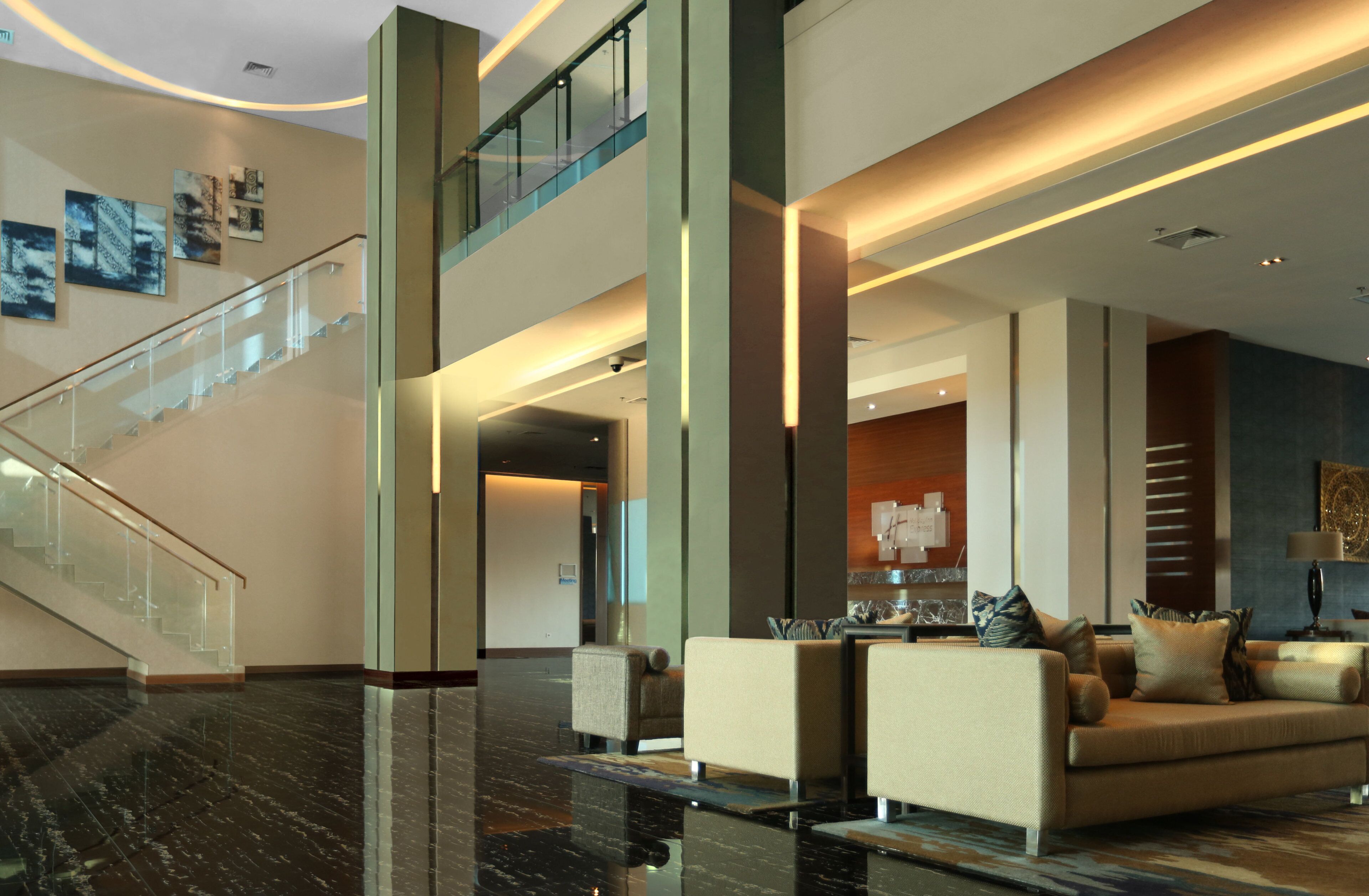 A modern lobby with a glass staircase, a seating area with sofas and a coffee table, and a reception desk.