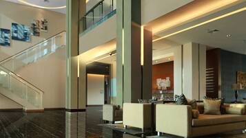 A modern lobby with a glass staircase, a seating area with sofas and a coffee table, and a reception desk.