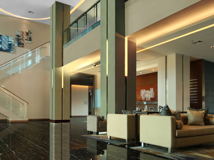 A modern lobby with a glass staircase, a seating area with sofas and a coffee table, and a reception desk.