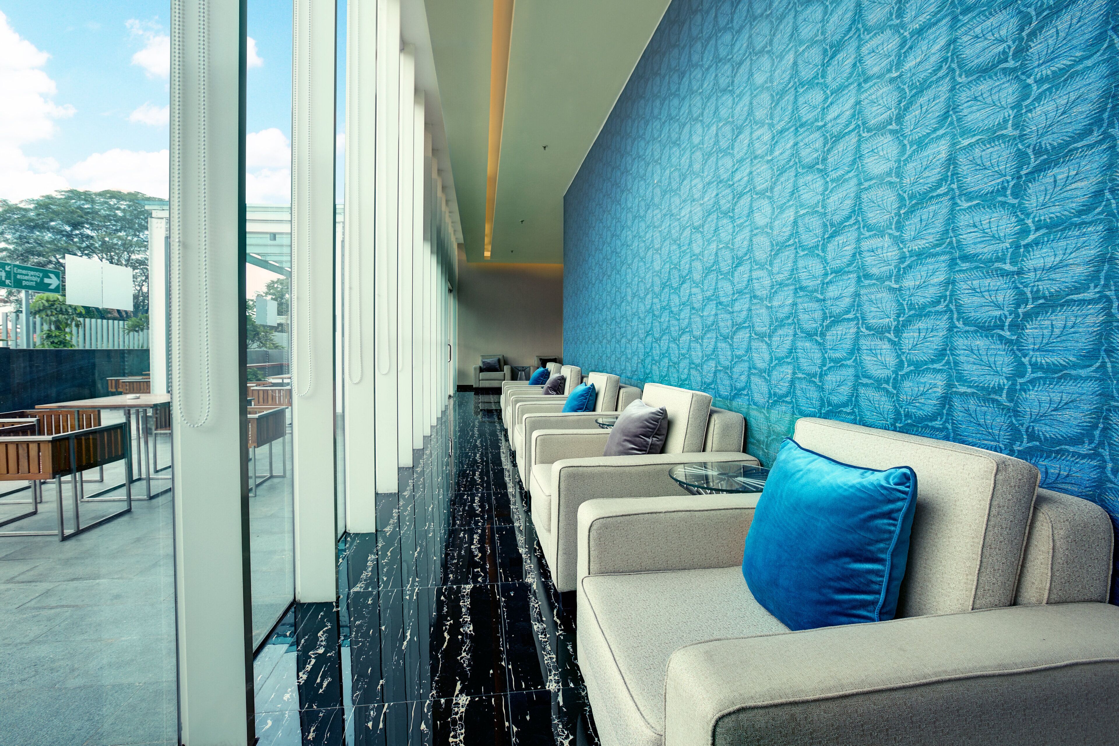 A hotel lobby with a long row of seating, a patterned wall, and a view of the outdoors.