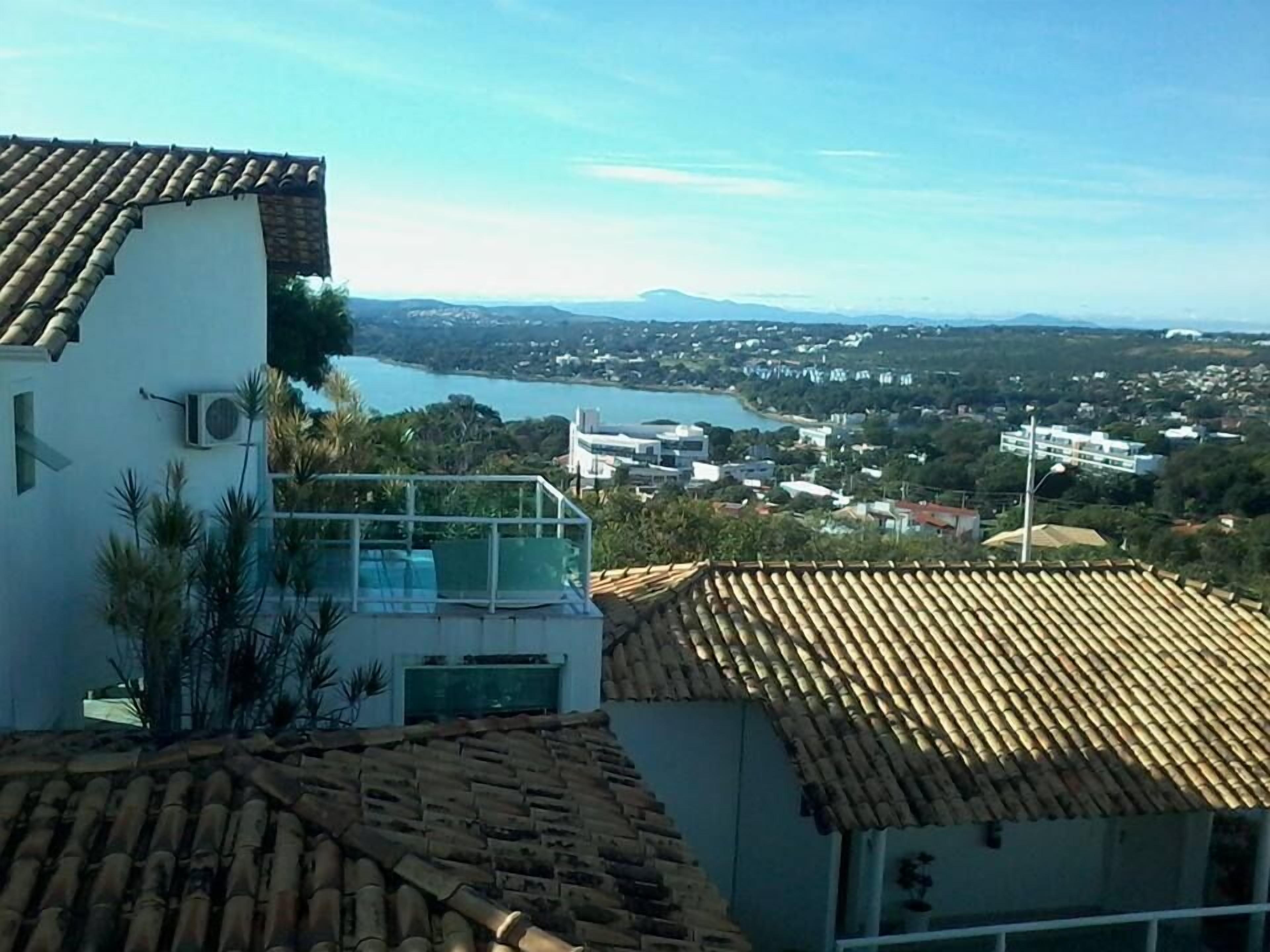 A residential building with a tiled roof, a balcony with glass railings, and a view of a lake and town in the distance.