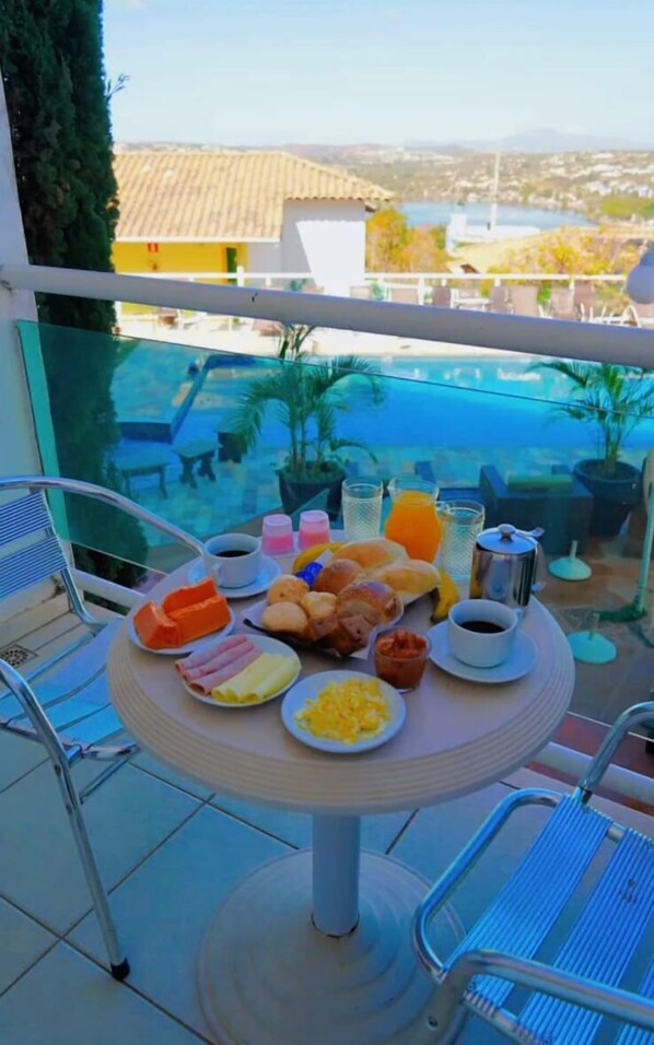 A table with breakfast items and a view of a swimming pool and buildings.
