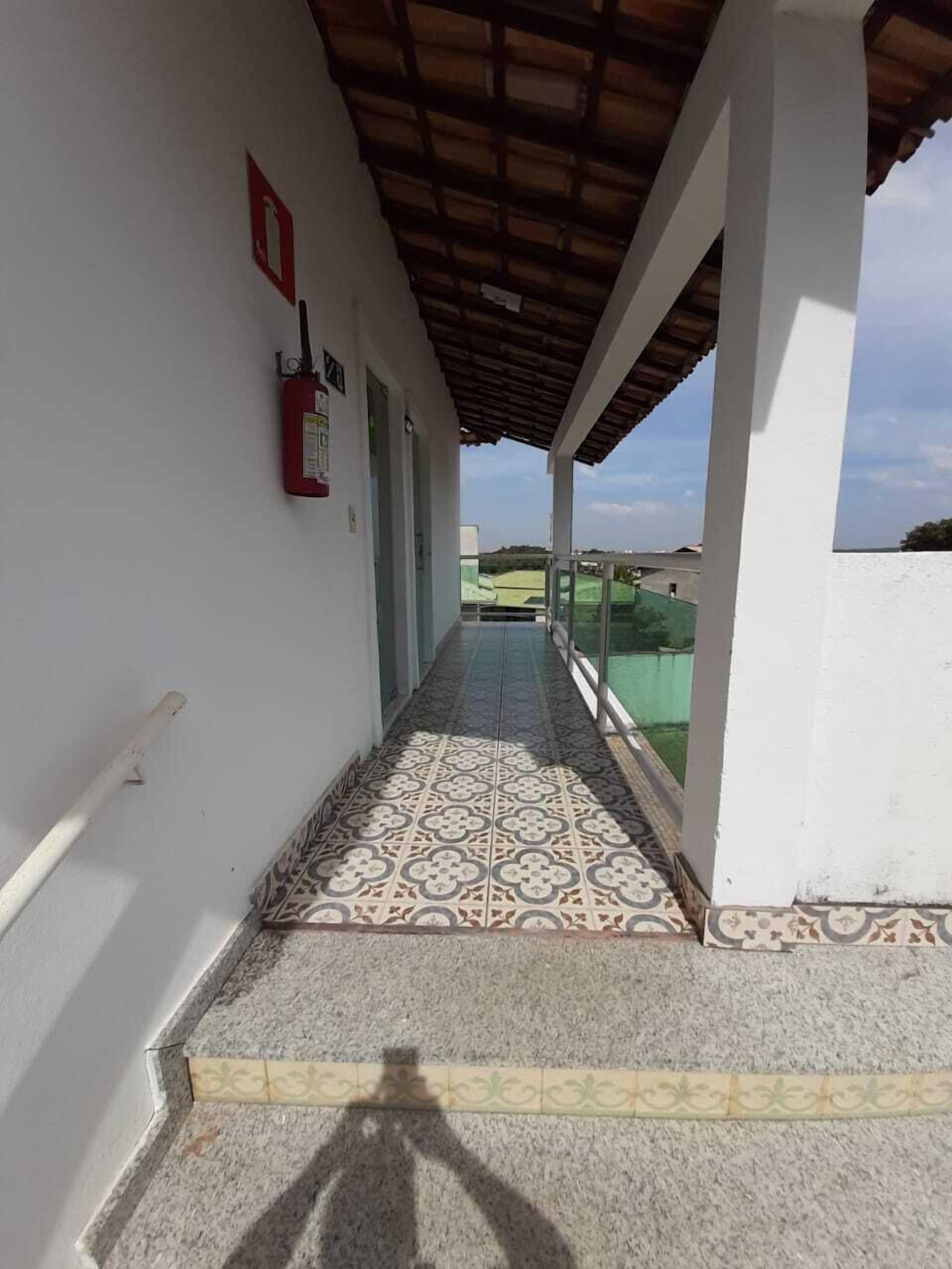 A corridor with patterned floor tiles, a fire extinguisher, and a view of a green field.