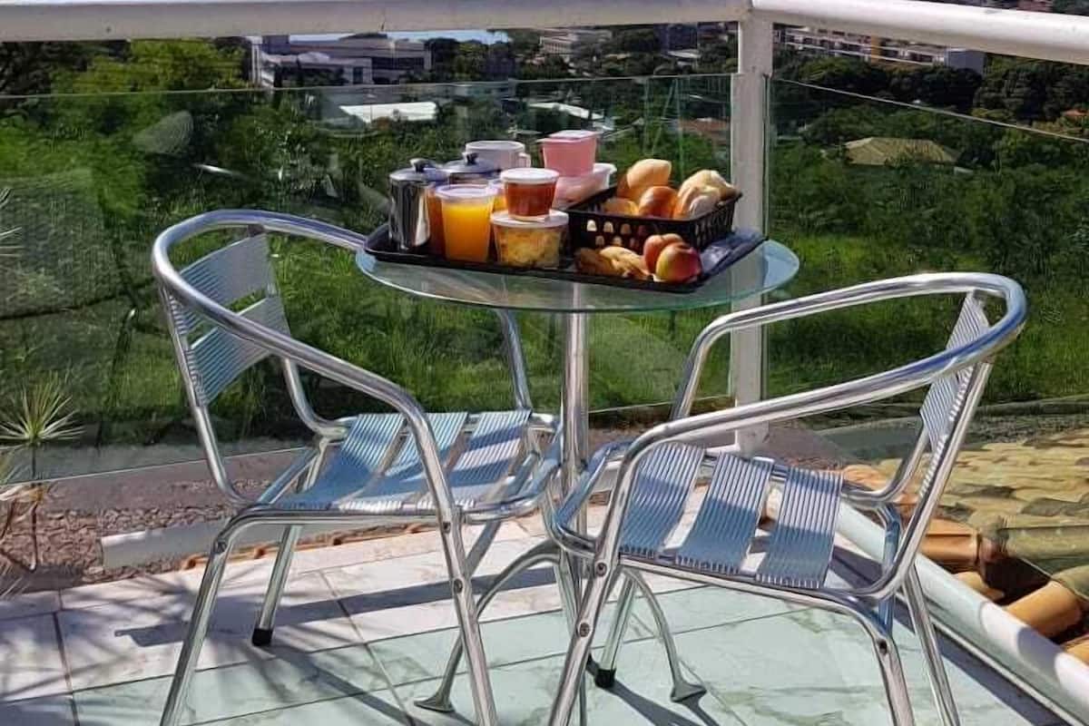 Mesa de vidro com cadeiras numa varanda com vista para a paisagem urbana.