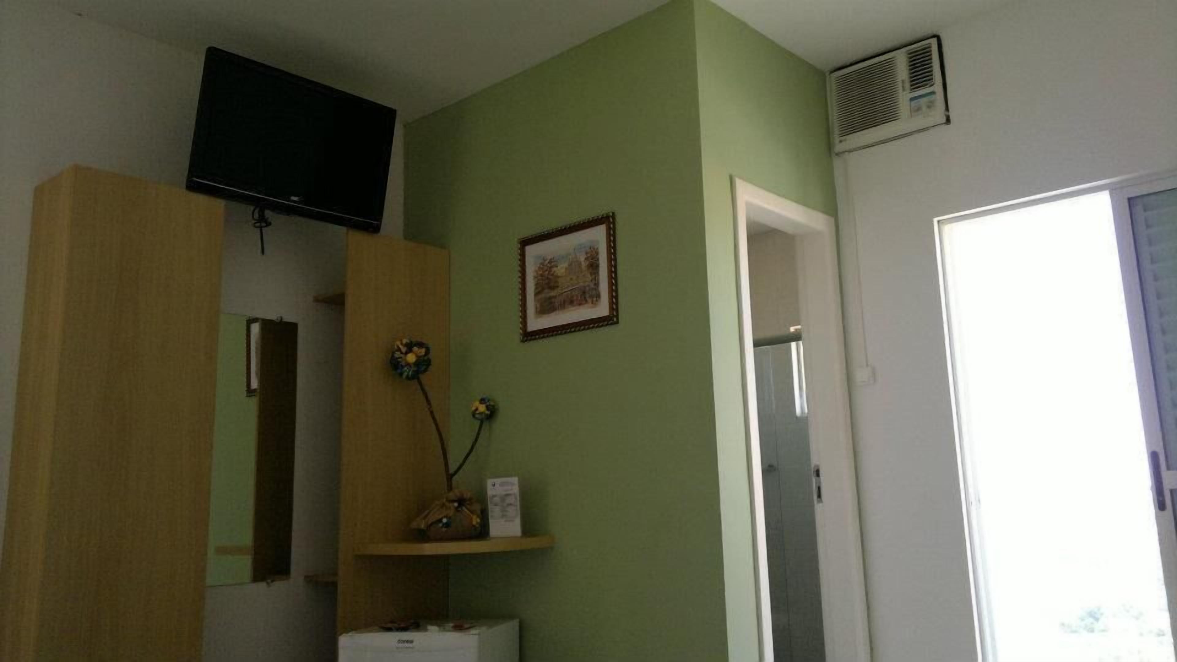 A room with a television mounted on the wall, a framed picture, a wooden wardrobe, and a door leading to another room.