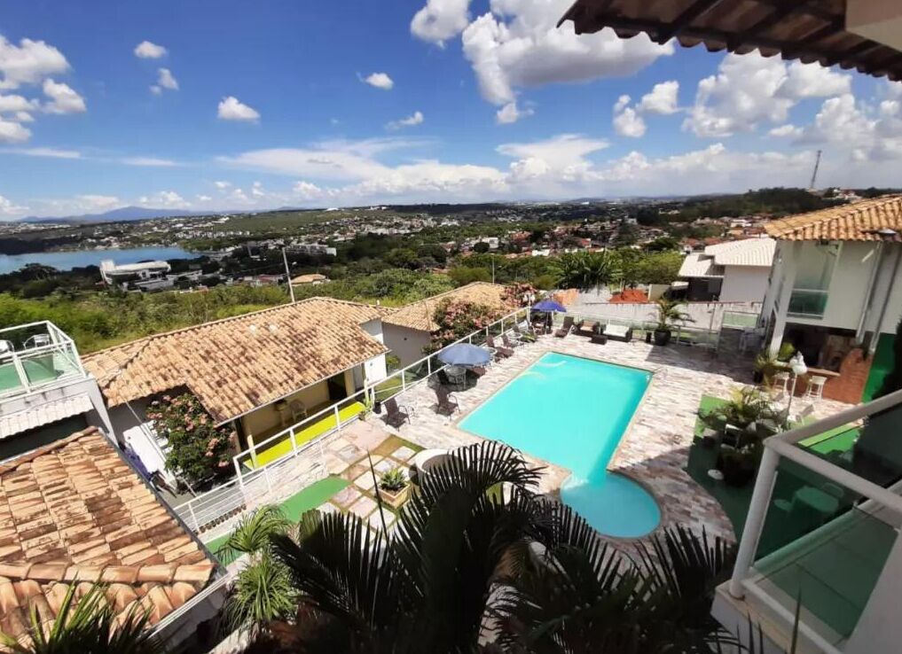 A pool area with a large pool, lounge chairs, and a view of a town and lake.