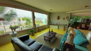 A living room with a black sofa, a blue sofa, a coffee table, and a statue. There are potted plants and a view of the outside. - Pousada Luak (Lagoa Santa)