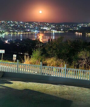 A nighttime view of a cityscape with a body of water reflecting city lights, a white railing in the foreground, and a sign with text.