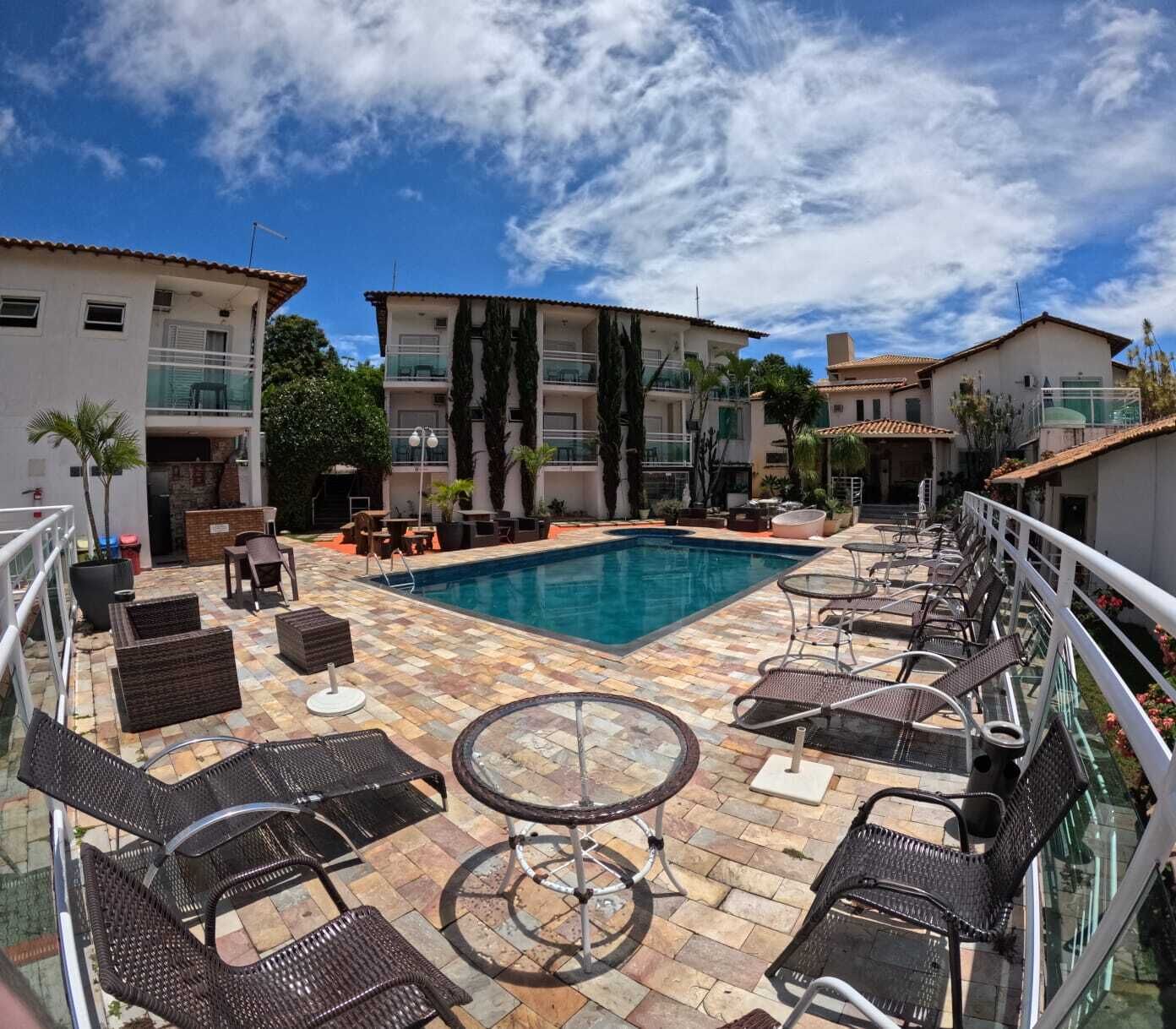 A rooftop pool area with lounge chairs and tables, surrounded by buildings.