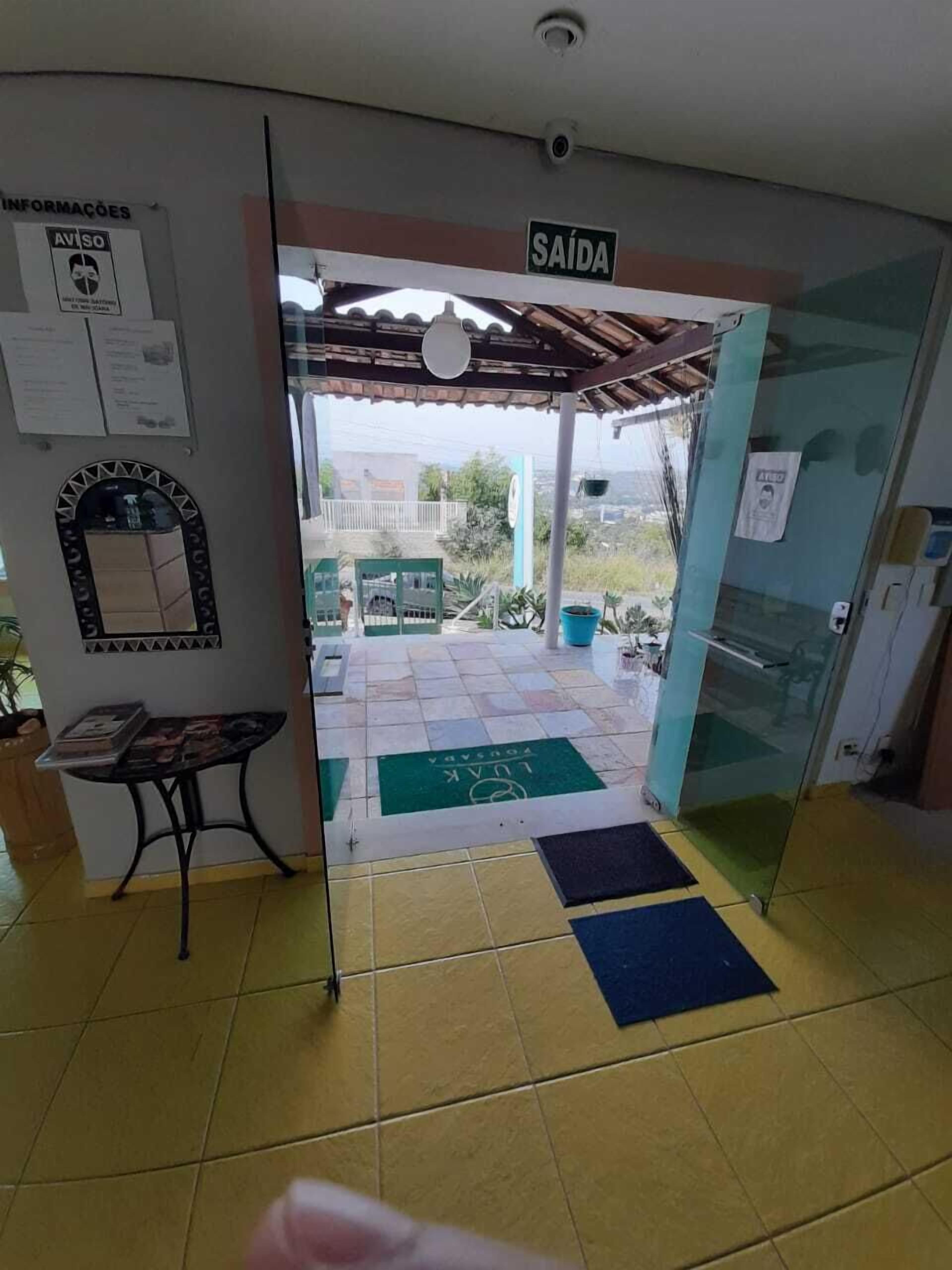 A reception area with a sign reading "SAÍDA" (exit), a tiled floor, a small table with magazines, and a glass door leading outside.