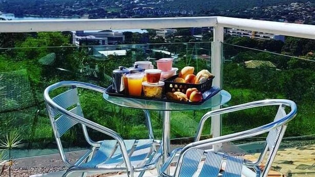 A balcony with a table set for breakfast, overlooking a cityscape with mountains in the distance. - Pousada Luak (Lagoa Santa)