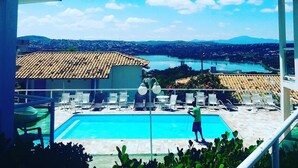 A swimming pool with lounge chairs, a clear sky, and a distant view of a town and mountains. - Pousada Luak (Lagoa Santa)