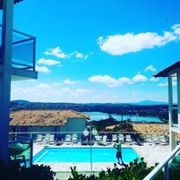 Una piscina con sillas de descanso, cielo despejado y una vista distante de un pueblo y montañas.