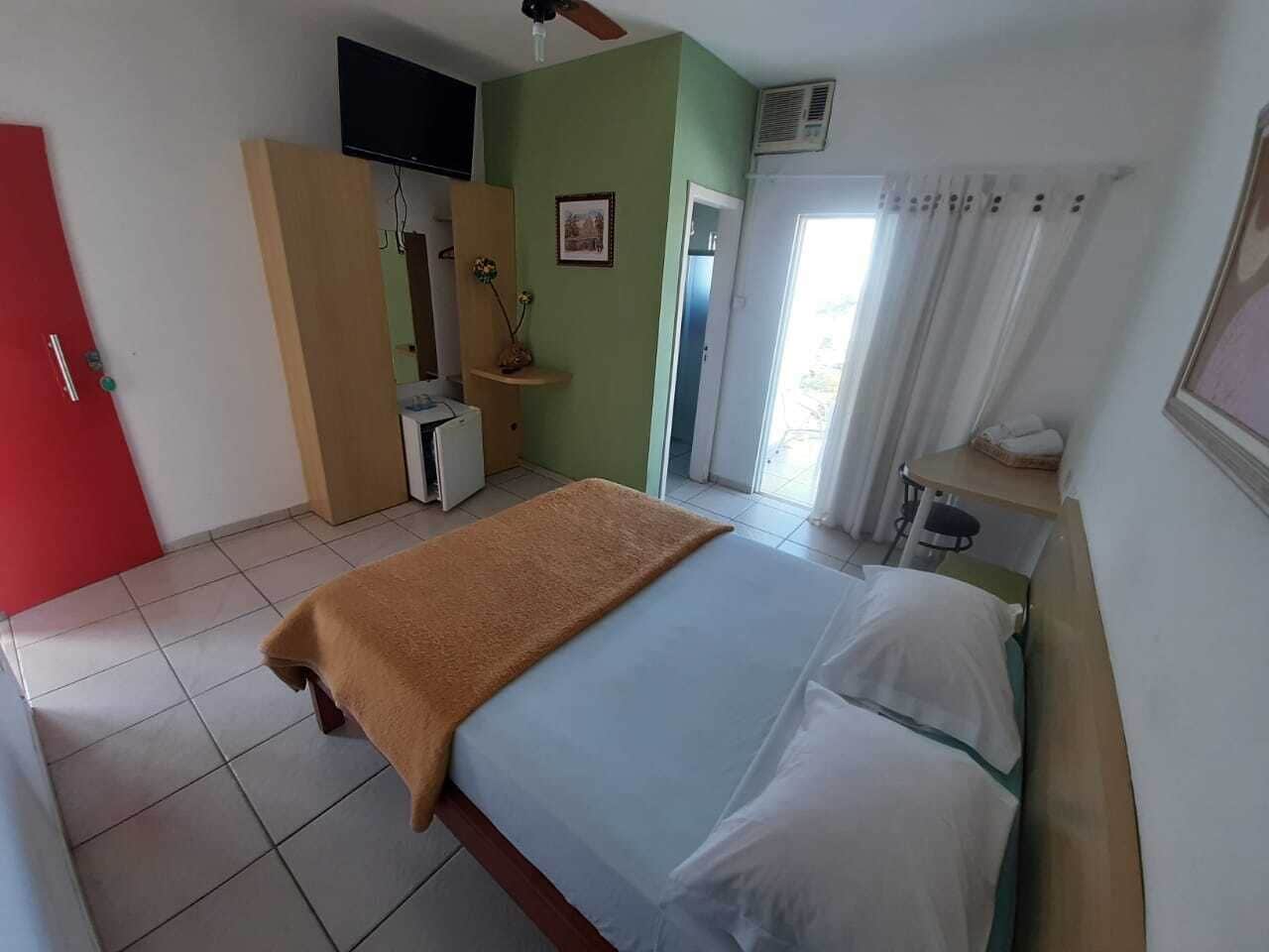 A hotel room with a bed, a TV, a desk, and a window with curtains.