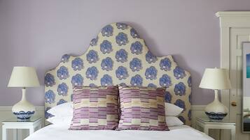 A neatly made bed with a patterned headboard, two bedside tables with lamps, and a wall with a floral wallpaper pattern.