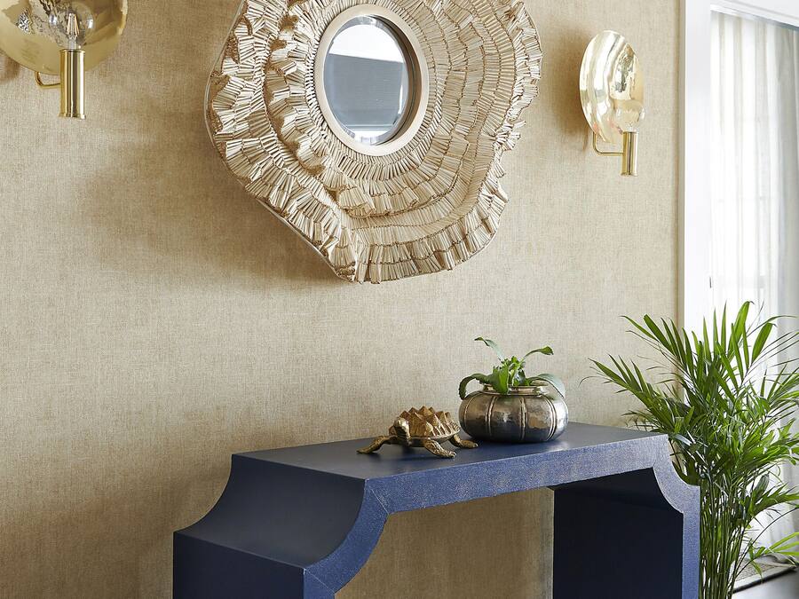 A room with a decorative mirror, a console table, and a potted plant.