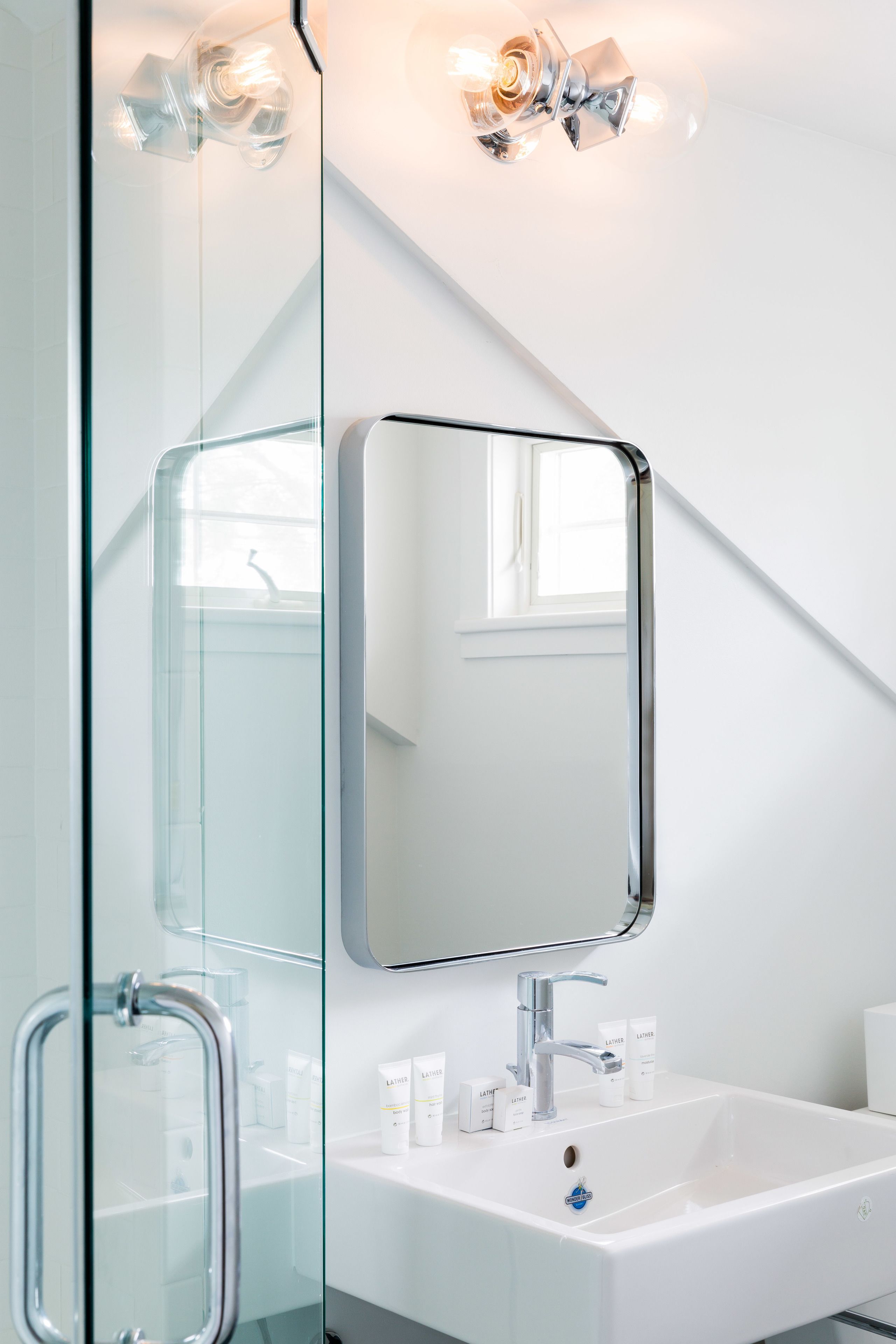 Un baño moderno con cabina de ducha de vidrio, un lavabo blanco con artículos de aseo y un espejo sobre el lavabo.