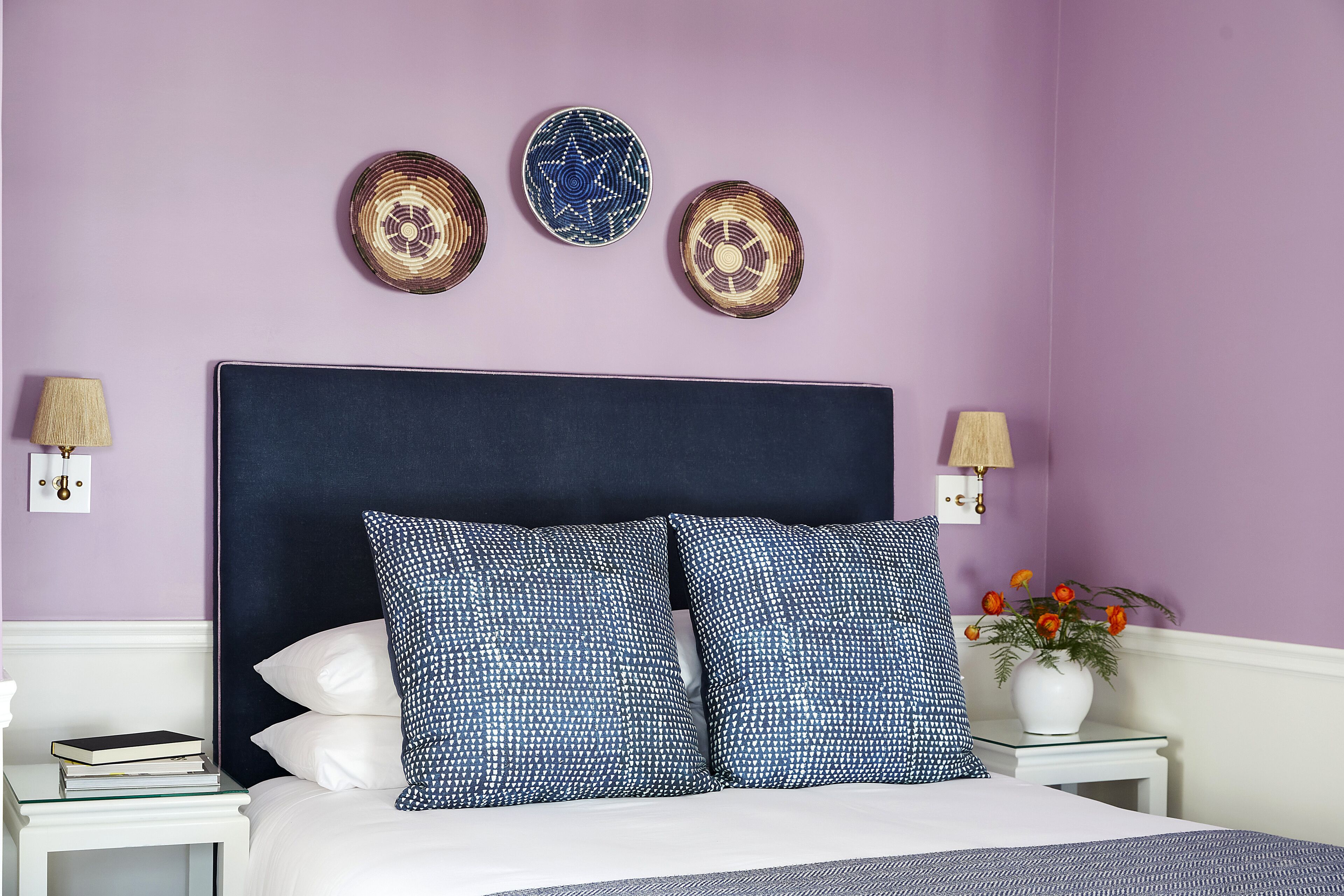 A bedroom with a bed, pillows, bedside tables, wall decorations, and a vase with flowers.