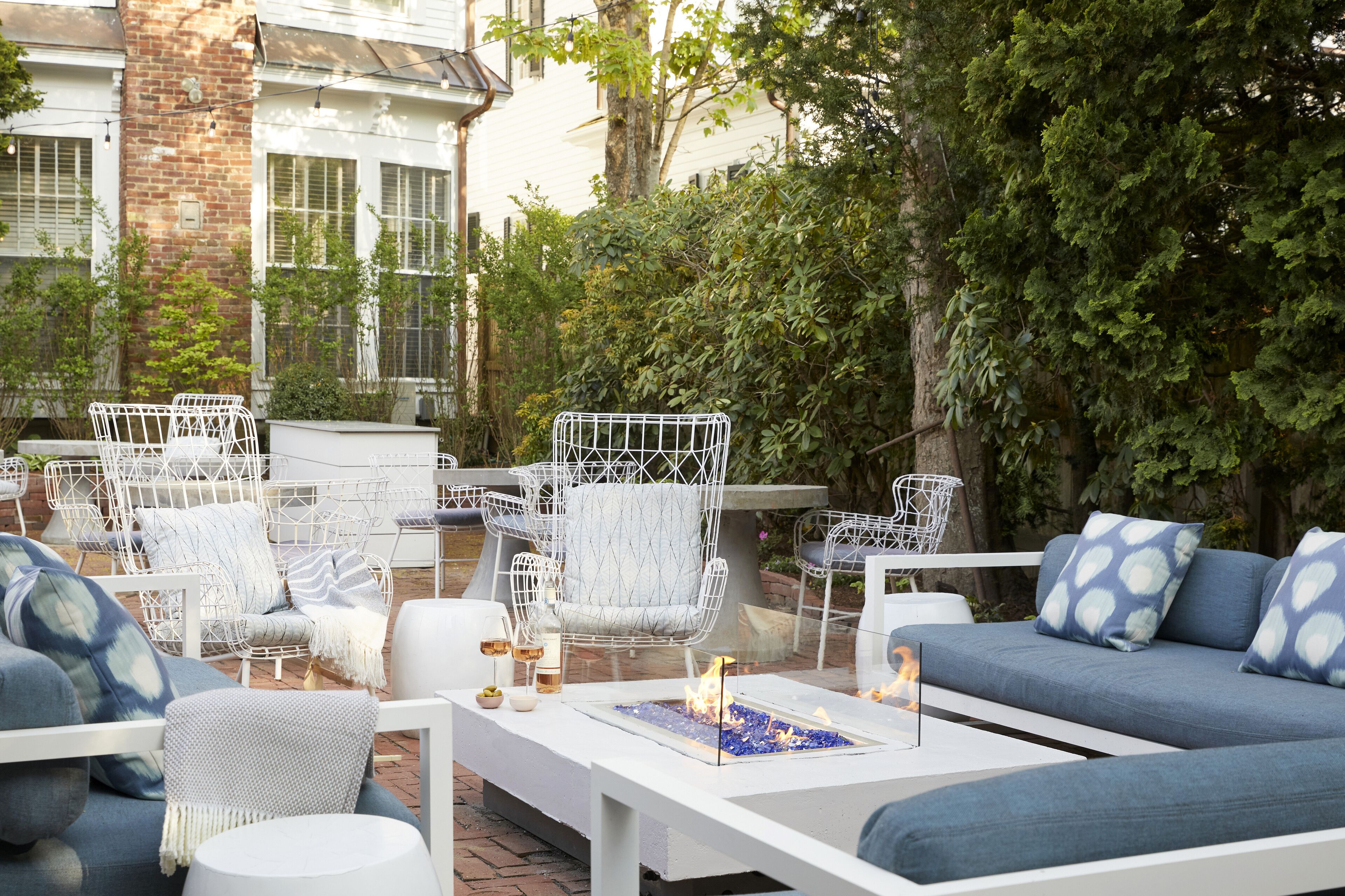 Un espacio de estar al aire libre con sillas de metal blanco, un sofá azul y una mesa blanca con chimenea.