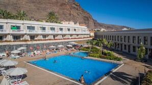 A hotel with a large pool area, multiple swimming pools, and a mountain backdrop. - Charco del Conde (Valle Gran Rey)