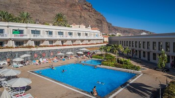 Una piscina al aire libre, sombrillas, sillones reclinables de piscina