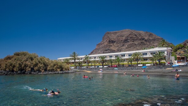 A beach resort with clear waters, palm trees, and a mountain in the background. - Charco del Conde (Valle Gran Rey)