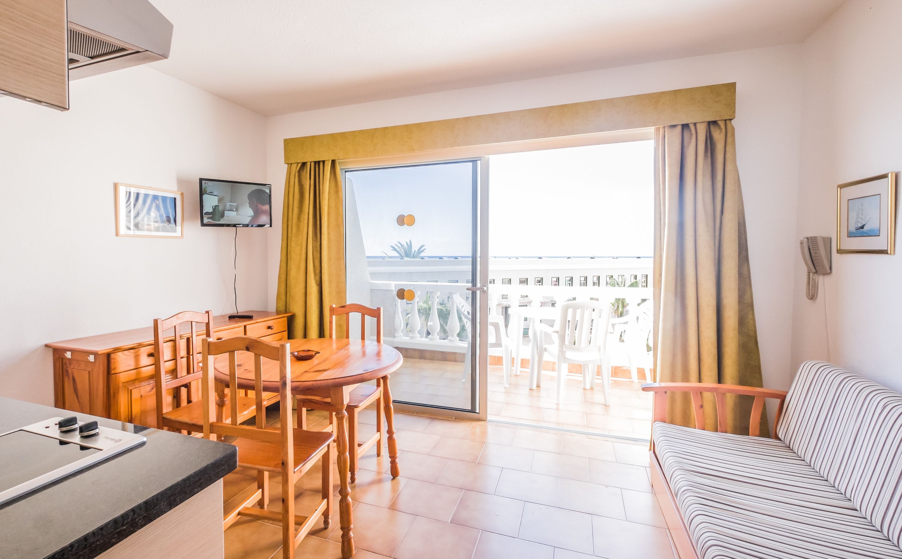 A hotel room with a dining area, a sofa, a TV, and a balcony with a view of the sea.