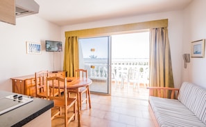 Habitació d'hotel amb zona de menjador, sofà, televisió i balcó amb vista al mar.