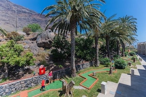 Un camp de golf amb palmeres, un turó rocos i un cel serè.
