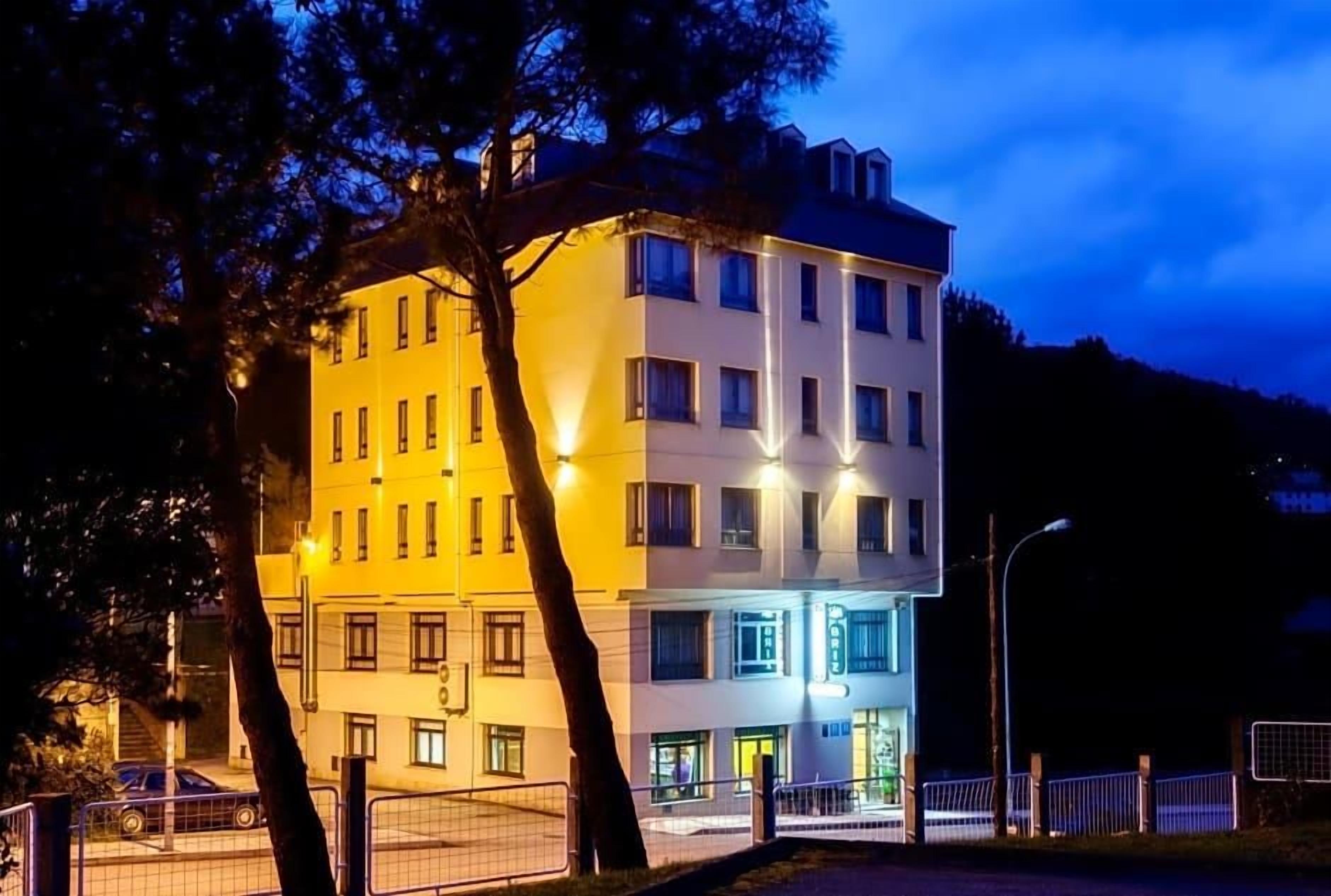 Un hotel de varios pisos con fachada blanca, múltiples ventanas y una entrada bien iluminada.