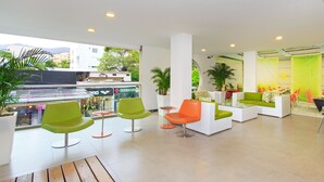 A modern indoor seating area with green and orange chairs, white sofas, and a glass table.