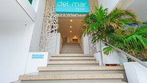 A staircase leading to the entrance of the Del Mar Hotel, with a sign above the door and a potted plant on the right.